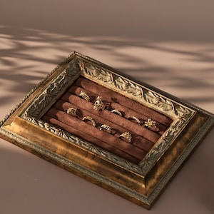A close-up of a vintage, baroque-style gold frame with a brown velvet interior used as a ring display tray.