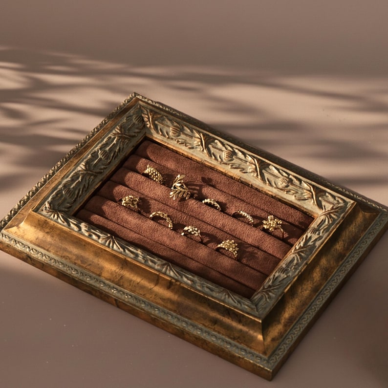 A close-up of a vintage, baroque-style gold frame with a brown velvet interior used as a ring display tray.