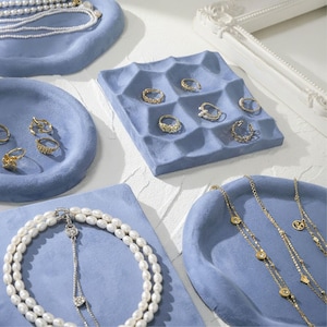 May include: A collection of jewelry display trays in various shapes and sizes. The trays are a soft blue color and hold rings, necklaces, and bracelets. The jewelry includes gold rings and necklaces with pearls and other gemstones.