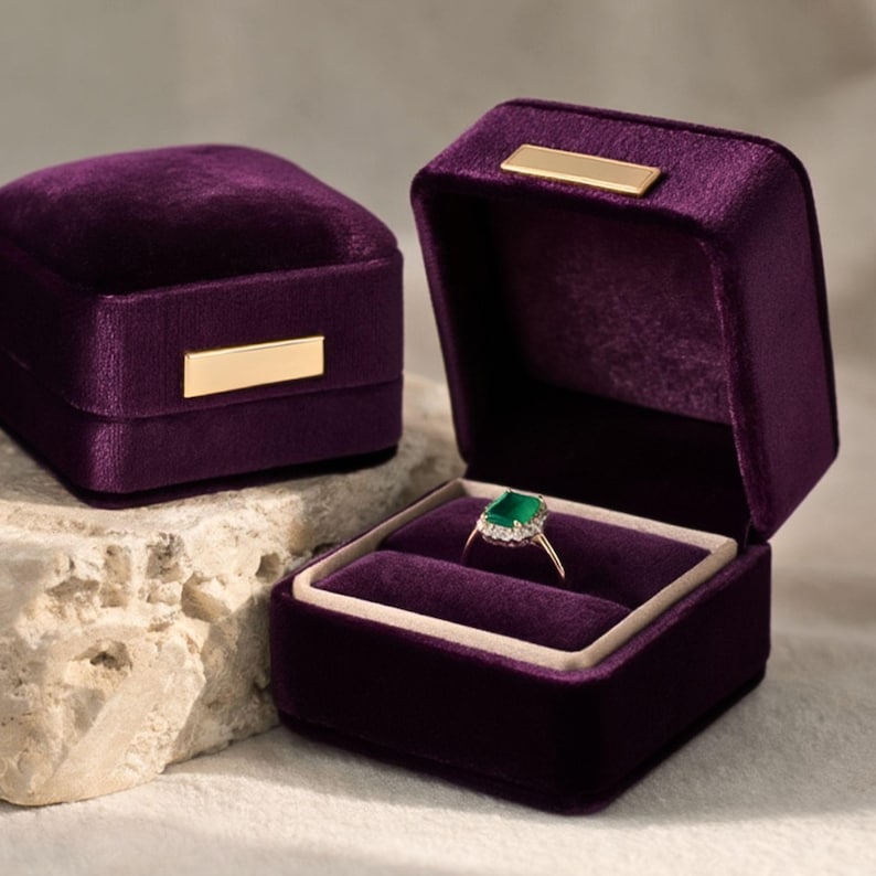 Pair of luxury violet purple velvet ring boxes. The open box showcases a diamond and emerald ring, creating a sophisticated look for jewelry branding or wedding detail shots.