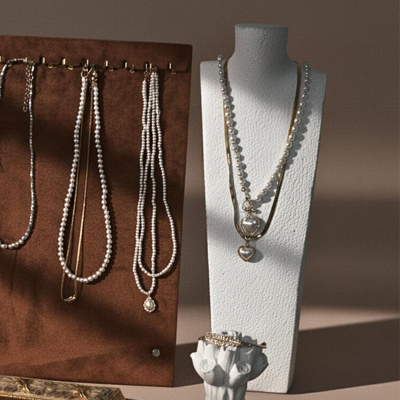 A jewelry display set featuring a brown velvet necklace board and a white mannequin bust, showcasing pearl and gold necklaces.