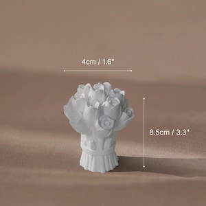 A white plaster sculpture of a rose bouquet used as a unique and aesthetic ring holder for multiple gold rings.