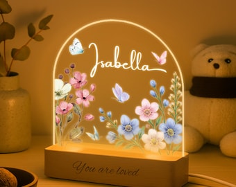 Może przedstawiać: Spersonalizowana lampka nocna z imieniem "Isabella" w ozdobnym piśmie, otoczona kwiatowymi i motylkowymi wzorami. Drewniana podstawa z napisem "You are loved". Światło emituje ciepły blask.