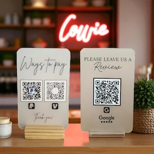以下が含まれることがあります： QRコードとテキストが記載された、2つのつや消しアクリルサイン。1つは「Ways to pay」と支払いロゴと「Thank you!」と書かれています。もう1つは「Please leave us a Review」とGoogleのロゴが書かれています。どちらも木製と透明アクリルのスタンドにあります。