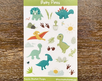 Op de afbeelding: Een vel stickers met schattige baby-dinosaurussen in verschillende poses. De stickers zijn op een witte achtergrond met groene accenten. De tekst "Baby Dinos" staat bovenaan het vel. De tekst "Katrina Abraham Designs" en "@katrinaabrahamdesign" staat onderaan het vel.