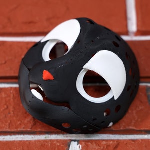 Puede incluir: Una máscara de animal negra y blanca con agujeros para los ojos y la nariz. La máscara está hecha de un material texturizado y tiene una nariz roja.