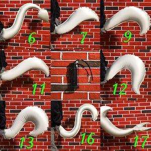 May include: A white inflatable tail with different poses, numbered 6, 7, 9, 11, 12, 13, 16, and 17. The tail is against a red brick wall.