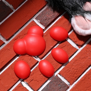 May include: Five red rubber paw prints on a brick wall background. The paw prints are in different sizes and shapes.