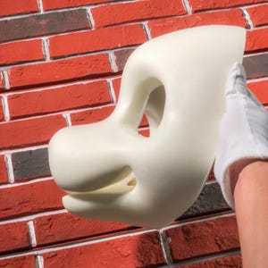 May include: A white foam blank fursuit head with a large, open mouth and two eye holes. The head is being held by a hand wearing a white glove.