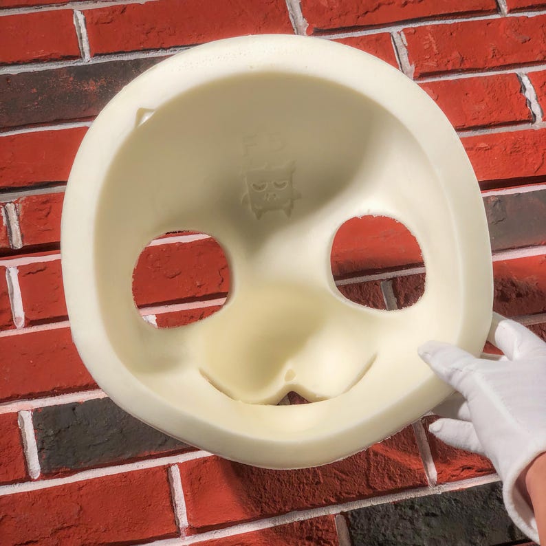 May include: White foam mask with eye and mouth cutouts. The mask has a small cartoon face with a frown on the top.