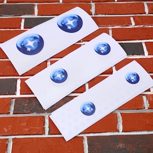May include: Four white sheets of paper with blue star stickers on them. The stickers are different sizes and are arranged in a decreasing size order.
