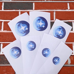May include: Seven white cards with a blue circle containing a crescent moon and three white stars. The cards are arranged in a fan shape against a brick wall background.