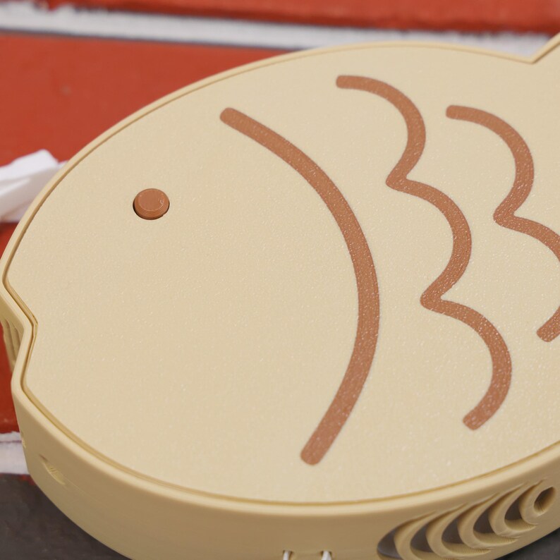 Taiyaki Fish Shaped Portable Fan with custom color options shown, highlighting the playful fish eye power button that adds a whimsical touch to this functional accessory. This 3D printed fan blends adorable aesthetics with practical cooling, offering three adjustable wind speeds to meet your needs. Its compact size and USB rechargeable design make it perfect for taking to summer festivals, gaming sessions, cosplay events, or even as a unique desktop gadget.