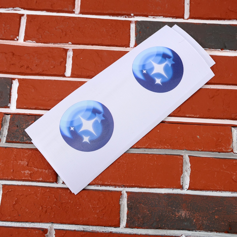 May include: Two white stickers with blue circles containing a white star design. The stickers are on a brick background.