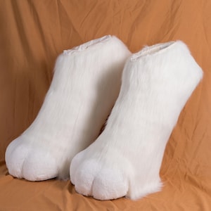 May include: A pair of white furry animal paws, likely for a costume. The paws are made of soft, plush fabric and have a realistic paw shape.