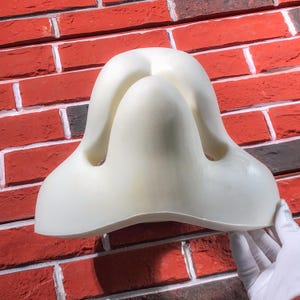 May include: White foam nose contouring tool for makeup application. The tool has two indentations for the nostrils and a raised center for the bridge of the nose.