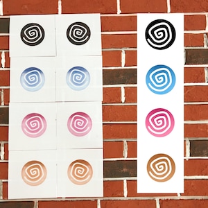 以下が含まれることがあります： 黒、青、ピンク、茶色の渦巻き模様が描かれた正方形の白いカードの配置。カードは赤いレンガの壁に配置されています。渦巻き模様は様々な色で、白い背景になっています。