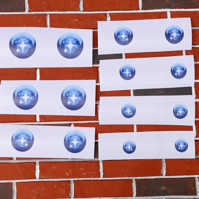 May include: A set of eight white rectangular stickers with a blue star design. Each sticker features a blue circle with a white star in the center. The stickers are arranged in rows on a brick wall.