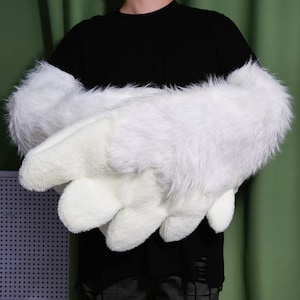 Op de afbeelding: Een paar witte, harige handschoenen met lange manchetten. De handschoenen hebben een klauwvormig ontwerp op de vingertoppen.
