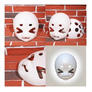 May include: White, oval-shaped mask with cut-out eye and mouth details, and a small nose. The mask has a cartoonish design, with angled cut-outs for the eyes and a small, curved mouth. The mask is displayed against a red brick wall.