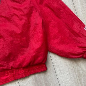 May include: A bright red vintage jacket with a zipper closure and elastic cuffs. The jacket has a logo on the upper left chest and a small logo on the sleeve. The fabric has a slight sheen.
