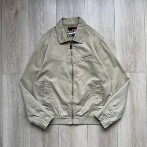 May include: A beige lightweight jacket with a zipper closure and a brand label on the left side of the chest. The jacket has two pockets on the front.