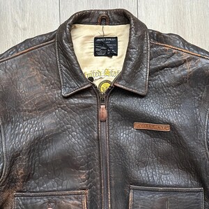 May include: A dark brown distressed leather bomber jacket with a cream-coloured interior lining. The jacket features a front zip closure, a fold-down collar, two front pockets, and a leather patch on the chest reading AVIREX LTD. A black label inside reads JACKET TYPE G-1.