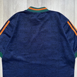 May include: A navy blue athletic shirt with orange stripes on the sleeves and a green and orange collar. The shirt has a speckled pattern and short sleeves. The shirt is made of a soft, comfortable material.