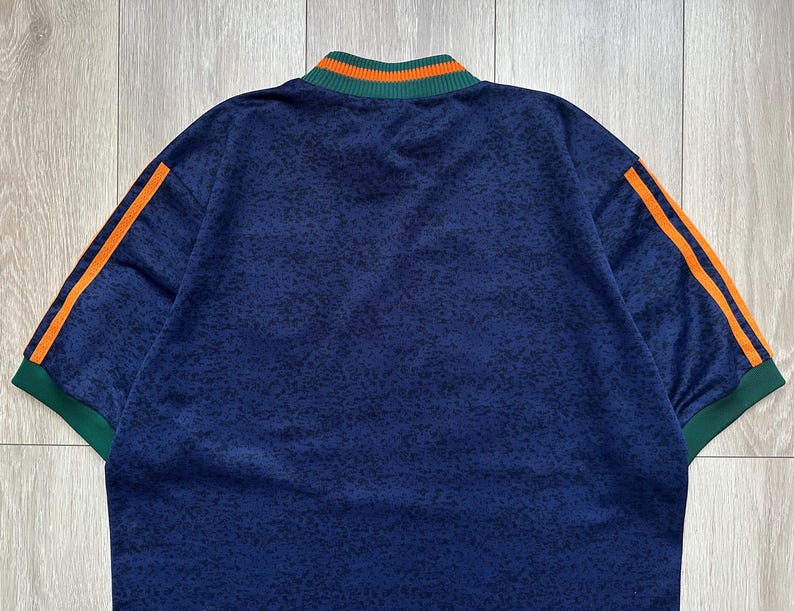 May include: A navy blue athletic shirt with orange stripes on the sleeves and a green and orange collar. The shirt has a speckled pattern and short sleeves. The shirt is made of a soft, comfortable material.