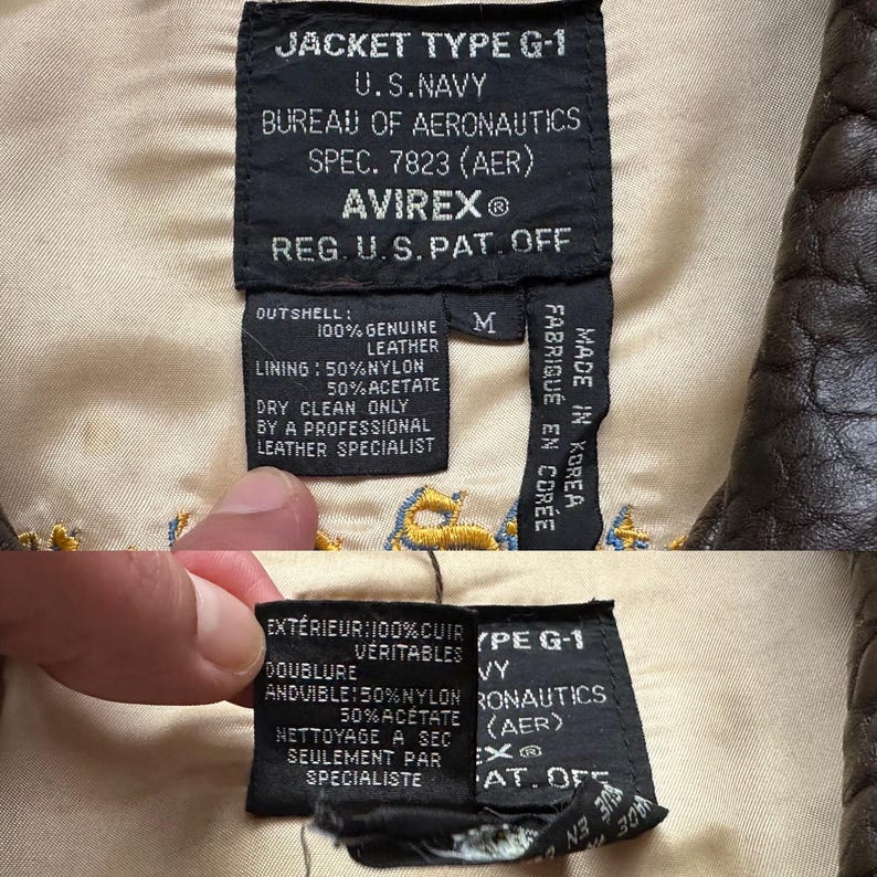 May include: A black rectangular garment label on a beige lining, reading JACKET TYPE G-1 U.S. NAVY BUREAU OF AERONAUTICS SPEC. 7823 (AER) AVIREX REG. U.S. PAT. OFF. The label details 100% genuine leather outshell, 50% nylon and 50% acetate lining, size M.