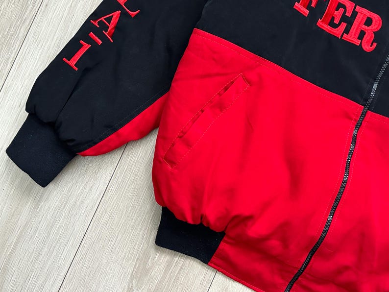 May include: A black and red jacket with the word "AFTER" embroidered in red on the upper back. The jacket has a black zipper and black cuffs. The sleeve has the word "LIFE" embroidered in red.
