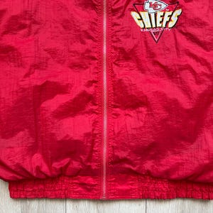 May include: A red nylon jacket with a full zipper and elastic cuffs and waist. The jacket features the Kansas City Chiefs logo on the upper left chest.