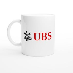 May include: White ceramic mug with a black and red UBS logo. The logo features a cluster of keys and the letters "UBS" in a bold, red font. The mug has a curved handle and a glossy finish.