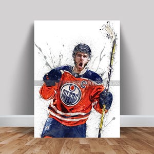 May include: A hockey player wearing an orange and blue jersey with the word "Oilers" on the front, raises his stick in the air. The player is wearing a helmet and has a determined expression on his face. The background is a white canvas with splashes of paint.