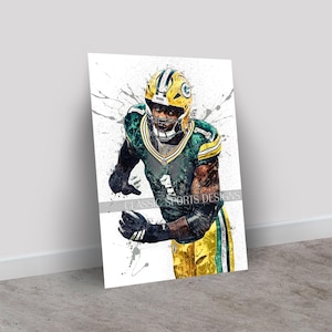 May include: A framed art print featuring a football player in a green and yellow uniform, with a helmet. The artwork has a watercolor-style effect with paint splatters. The text "CLASSIC SPORTS DESIGNS" is visible.