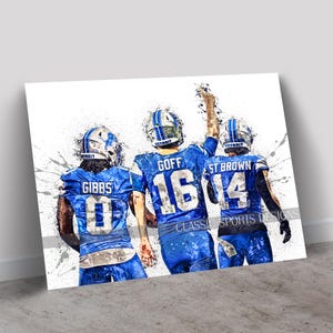 May include: Four football players in blue uniforms with white numbers and white helmets. The players are standing together with their arms around each other. The background is a white splatter pattern. The players' names and numbers are visible: Gibbs 0, Goff 16, St. Brown 14.