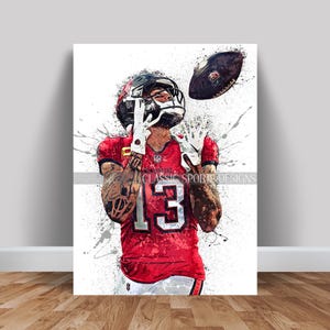 Peut inclure: Une peinture numérique d'un joueur de football portant un maillot rouge avec le numéro 13, un casque noir et des gants noirs. Le joueur attrape un ballon de football et a une expression déterminée sur son visage. L'arrière-plan est blanc avec des éclaboussures de peinture.