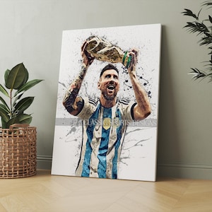 K&ouml;nnte beinhalten: Ein Aquarellbild eines Fu&szlig;ballspielers, der eine goldene Troph&auml;e hochh&auml;lt. Der Spieler tr&auml;gt ein blau-wei&szlig; gestreiftes Trikot mit der Nummer 10. Der Hintergrund ist ein wei&szlig;es Spritzmuster.