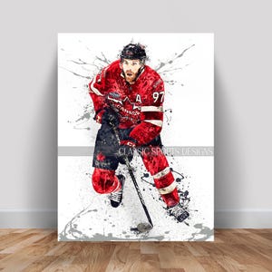 May include: A watercolor-style print of a hockey player in a red and white Canada jersey with the number 97. The player is in action, skating with a hockey stick, with paint splatters in the background. The text "CLASSIC SPORTS DESIGNS" is visible.