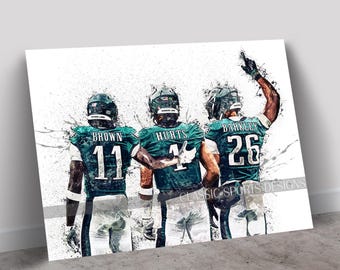 May include: Three American football players in green and white uniforms with their numbers visible. The players are in a dynamic pose, with the player on the right raising his arm in the air. The background is a white splatter effect.