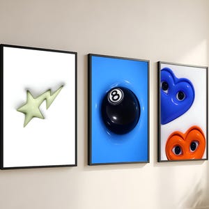 Peut inclure: Trois impressions d'art encadrées exposées sur un mur. Les impressions présentent une étoile vert clair, une boule noire numéro 8 dans un liquide bleu et deux cœurs de dessins animés. Les cadres sont noirs et le mur est blanc.