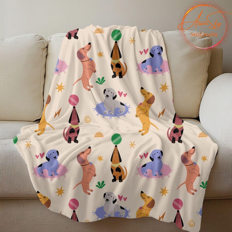 May include: A cream-colored fleece blanket with a repeating pattern of cartoon dachshunds in various colors, holding balls and hearts. The dachshunds are on a cream background with stars, hearts, and swirls.