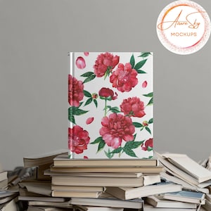 May include: A white notebook with a floral pattern of pink peonies and green leaves. The notebook is sitting on a stack of books.
