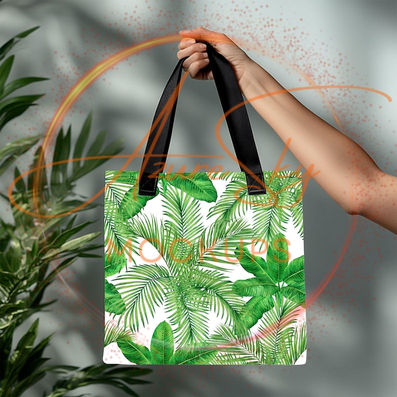 May include: A white tote bag featuring a tropical leaf pattern. The bag has black handles and is made from a durable fabric.