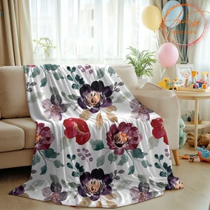 May include: A white throw blanket with a watercolor floral pattern featuring burgundy, purple, and red flowers with green leaves.