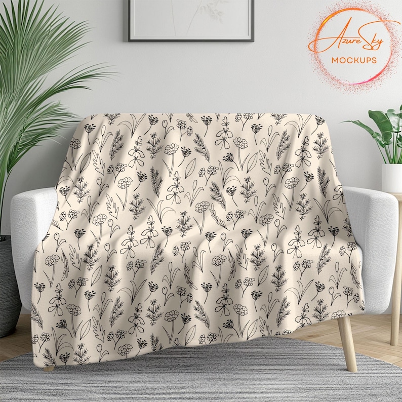 May include: A cream-colored throw blanket with a black and white floral pattern. The blanket is draped over a white couch.