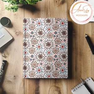 May include: A white notebook with a colorful floral pattern. The notebook is closed and lying flat on a wooden surface.
