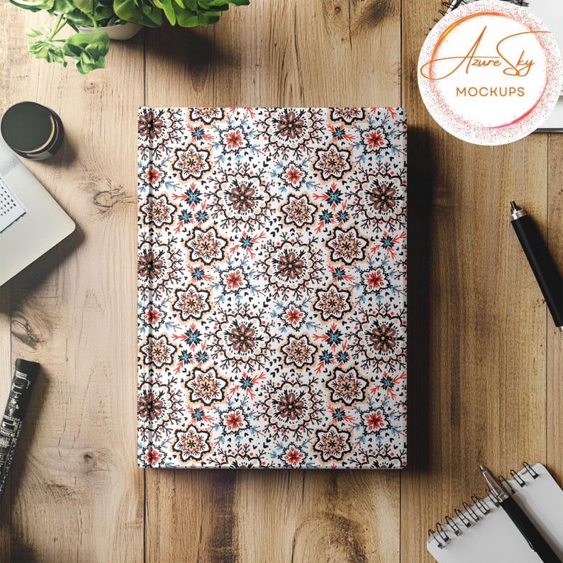 May include: A white notebook with a colorful floral pattern. The notebook is closed and lying flat on a wooden surface.