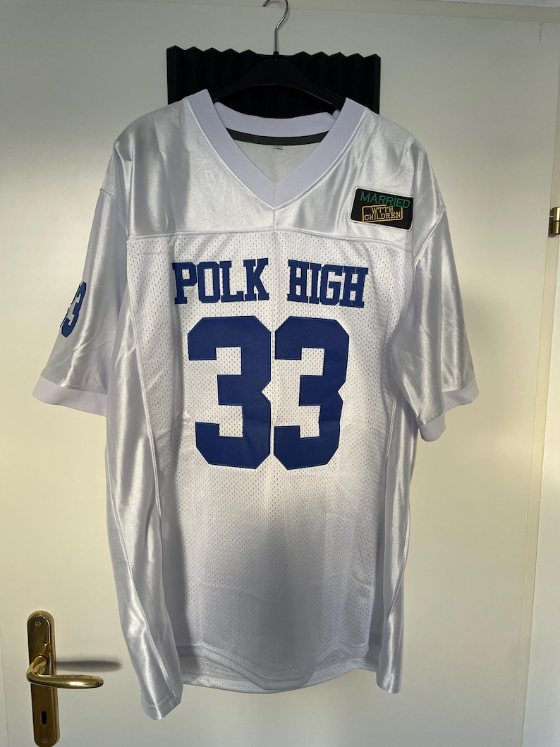 May include: White football jersey with blue lettering that reads "POLK HIGH 33". A small patch with the text "MARRIED WITH CHILDREN" is on the upper right side of the jersey.