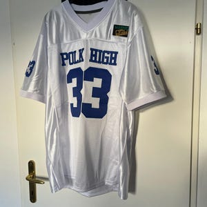 May include: White football jersey with blue lettering that reads "POLK HIGH" and the number "33". A small green patch with the text "MARRIED WITH CHILDREN" is on the right side of the jersey.